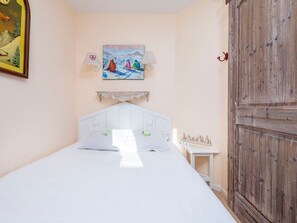 Une chambre à coucher avec un lit blanc, un tableau représentant des skieurs, une armoire en bois et une petite table de chevet.