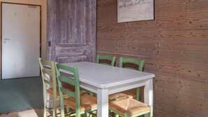 A dining area with a white table and green chairs, wooden walls, a door, and a painting. - Charming renovated apartment 2 rooms, balcony, WiFi (Avoriaz)
