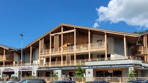 A multi-story building with wooden balconies and stone facade, featuring shops and signage for local businesses. - Luxury central apartment - 6 pers, parking, wifi (Les Gets)