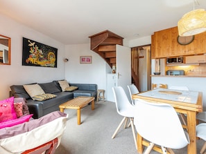 A modern living room with a sofa, coffee table, and dining table with chairs. There is a staircase leading to a kitchen area with a microwave and toaster.