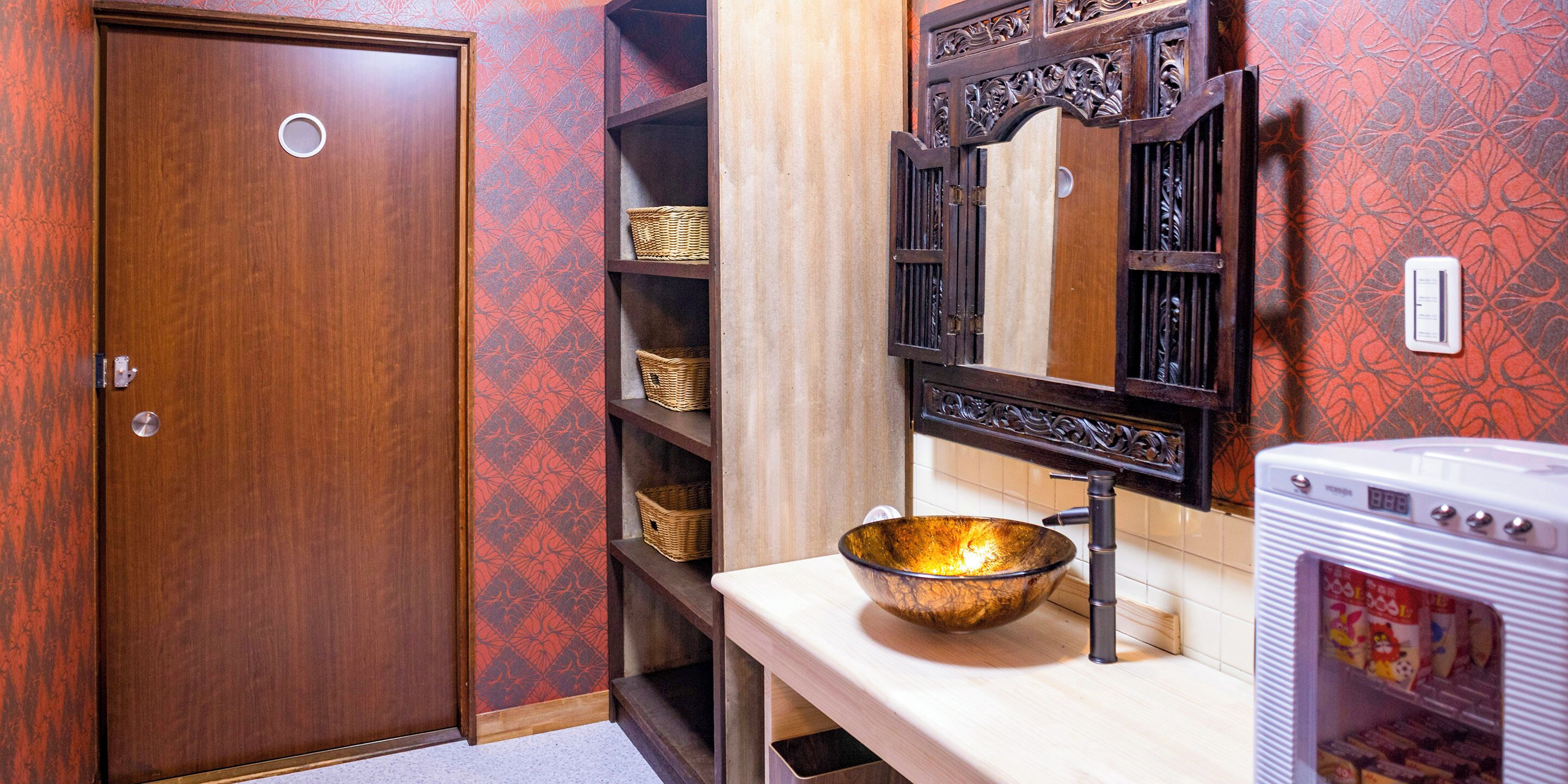A bathroom with a wooden door, a sink with a decorative bowl, a mirror with an ornate frame, and shelves with baskets.