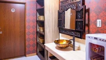 A bathroom with a wooden door, a sink with a decorative bowl, a mirror with an ornate frame, and shelves with baskets.