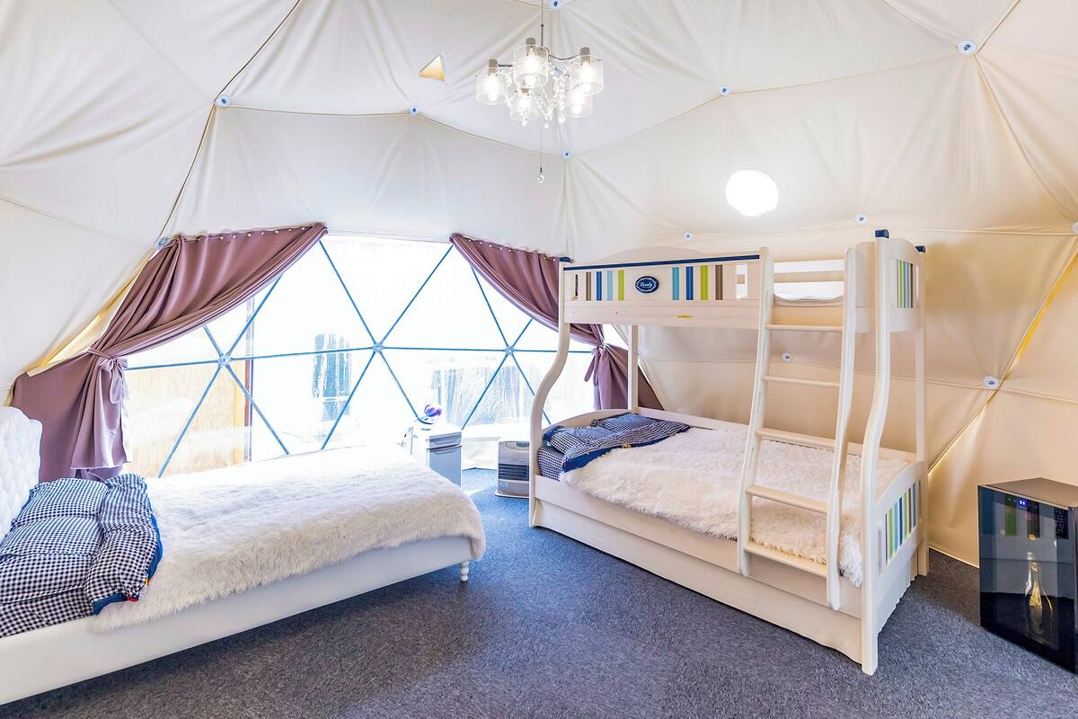 Una habitación con carpa que tiene dos camas, un candelabro y un dispensador de agua.
