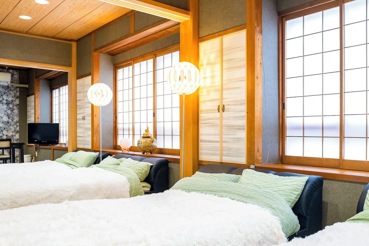 Una habitación tradicional japonesa con suelo de tatami, una mesa baja con televisor y un ventanal grande con puertas correderas shoji.