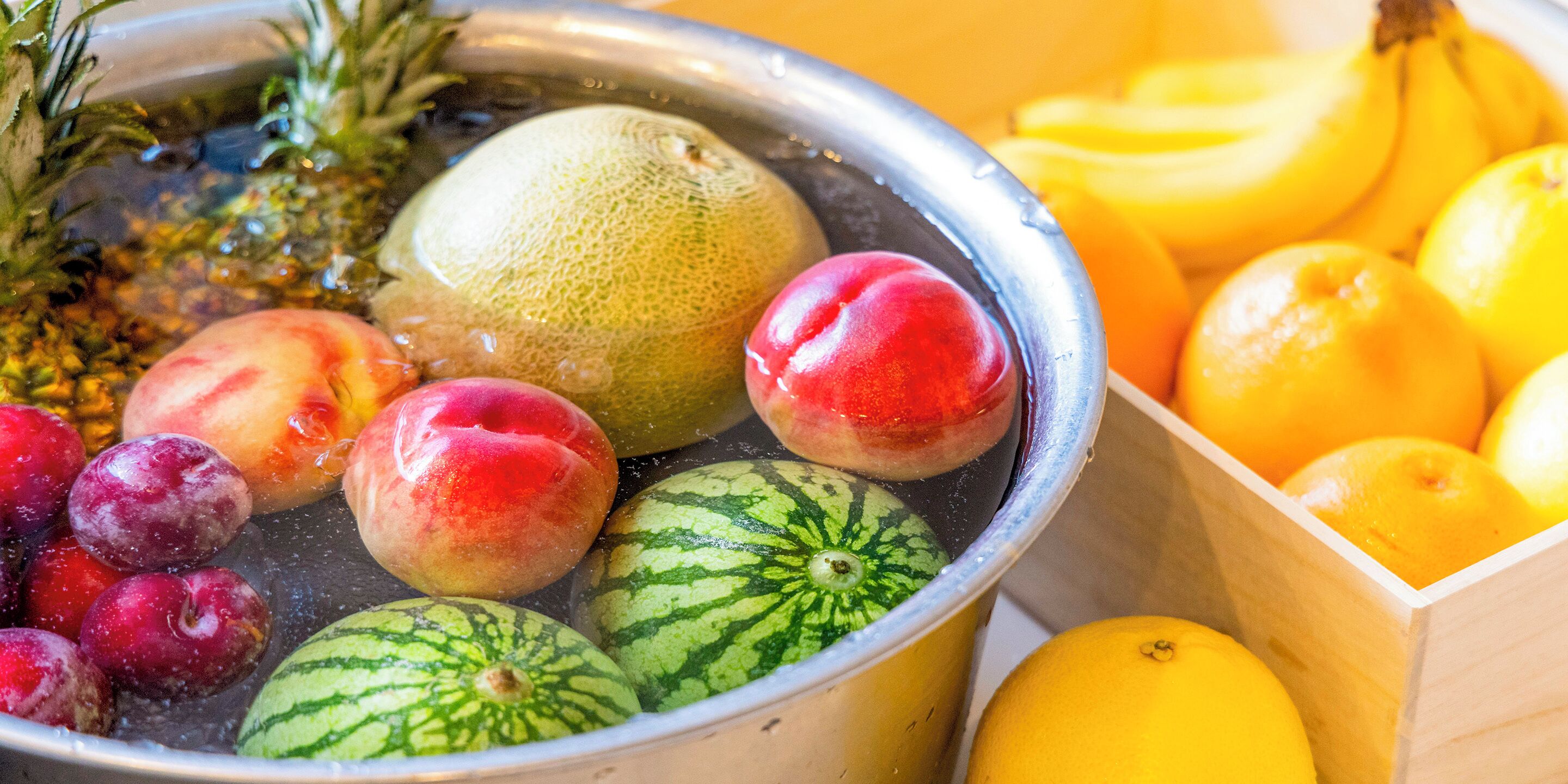Eine Schüssel mit frischen Früchten, darunter Wassermelonen, Pfirsiche, Pflaumen und eine Ananas.