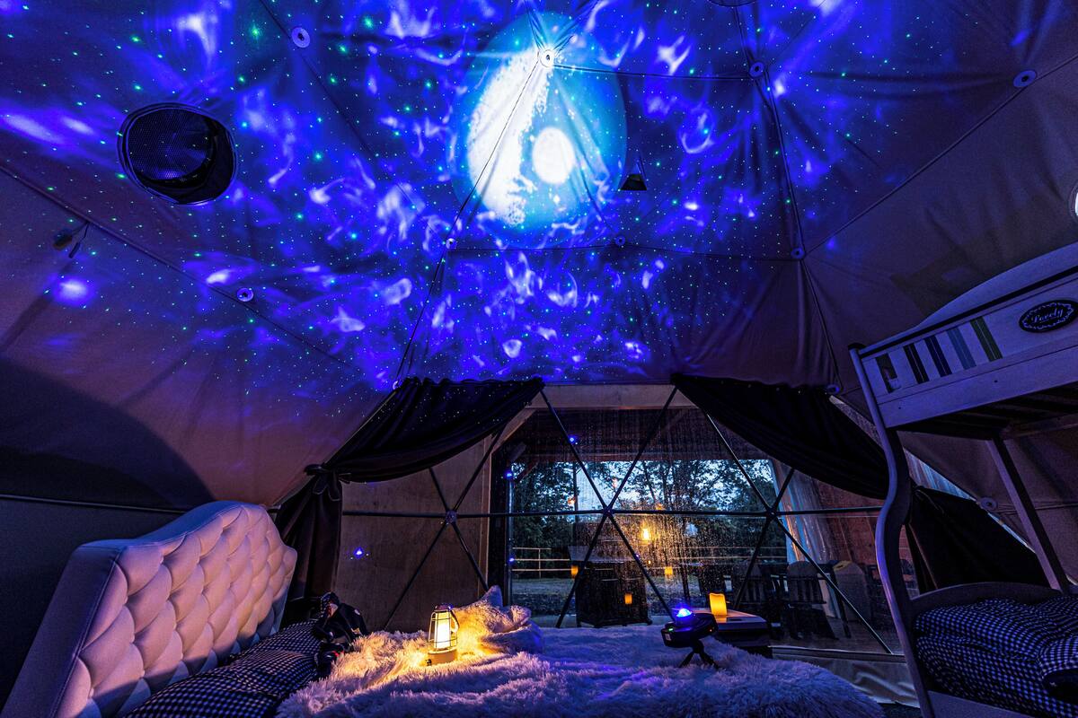 Alojamiento en tienda de campaña con proyección de cielo estrellado, una cama acogedora y vistas al exterior.
