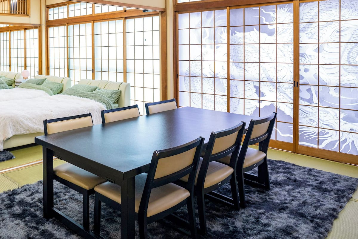 Una habitación japonesa tradicional con suelo de tatami, una mesa baja con sillas y un futón como cama.