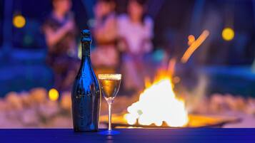 A bottle of Bottega wine and a glass of wine on a table with a fire in the background.