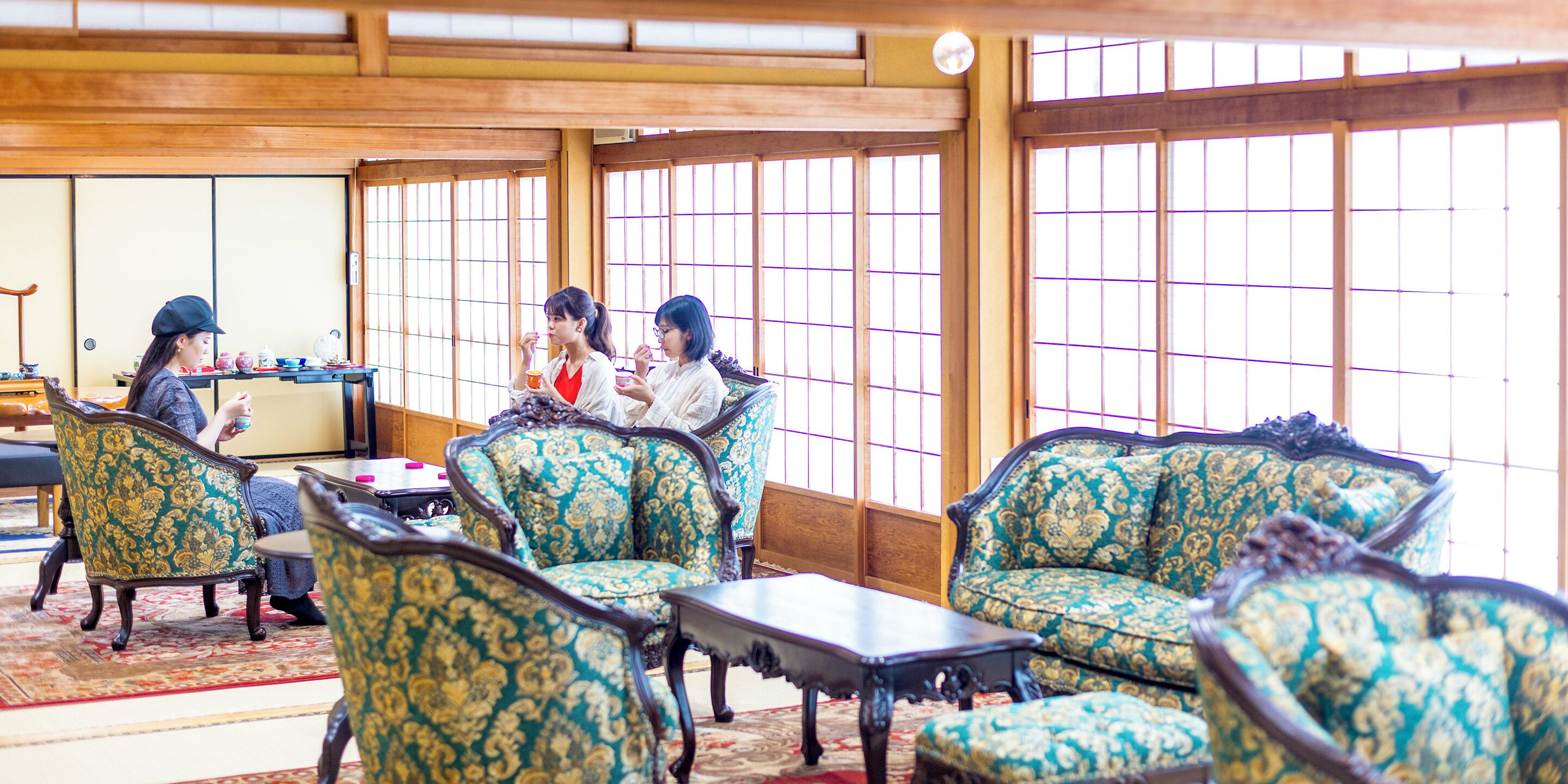 A traditional Japanese-style room with tatami mat flooring, low wooden tables, and green patterned furniture.