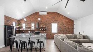 Een moderne keuken met een bakstenen muur, een centraal eiland met barkrukken, een ingebouwde oven en een groot raam.