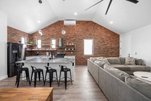 A modern kitchen with a brick wall, a central island with bar stools, a built-in oven, and a large window. - The Haven -two kitchens, pool, large garage, minutes from the dunes. (Hurricane)