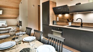 A modern kitchen with dark cabinetry, a wooden dining table set for four, and a built-in oven.