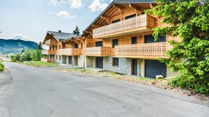 A row of wooden chalet-style buildings with balconies, set against a mountainous backdrop.