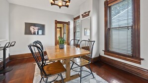 A dining room with a wooden table, black chairs, a chandelier, and a large window with blinds. - Unwind and indulge in this spacious and stylish Short North retreat. (Columbus)