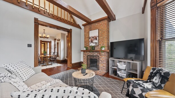 A living room with a sofa, armchair, TV, fireplace, and dining area. - Unwind and indulge in this spacious and stylish Short North retreat. (Columbus)