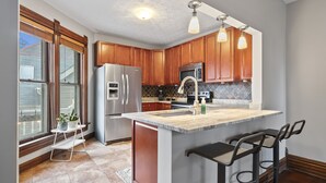A kitchen with wooden cabinets, stainless steel appliances, a marble countertop, and a bar area. - Unwind and indulge in this spacious and stylish Short North retreat. (Columbus)