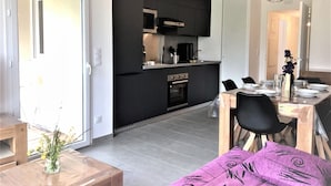 A modern kitchen with black cabinets, a built-in oven, and a dining area with a table set for four. - Modern apartment with terrace and private parking (Barcelonnette)