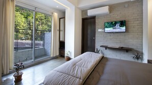 Un dormitorio moderno con una cama grande, un televisor montado en una pared de ladrillo y un ventanal corredero que da a un balcón.