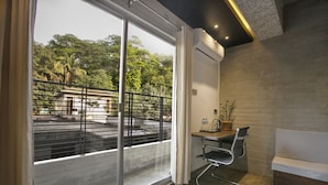 Una habitación moderna con un gran ventanal corredera que da a un balcón exterior, un escritorio pequeño con una silla, y un banco acolchado.