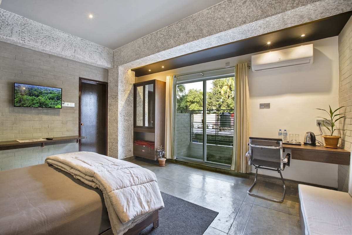 Ein modernes Hotelzimmer mit Bett, Schreibtisch, Fernseher und einer Schiebetür zum Balkon.