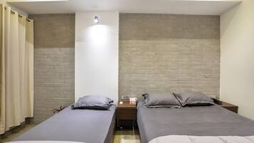 Quarto com duas camas de solteiro, uma mesa de cabeceira com abajur e parede de tijolos.