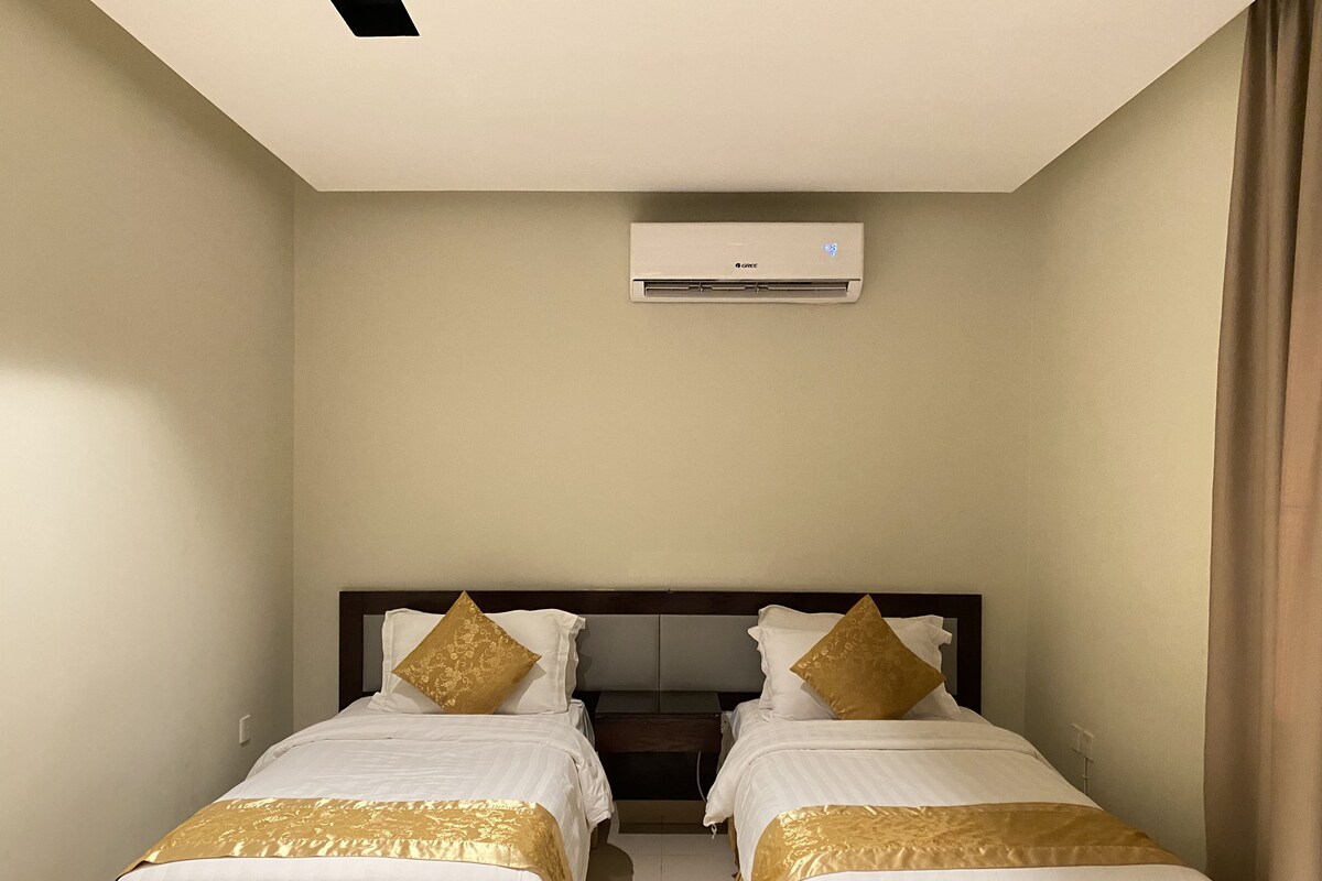 A hotel room with two single beds, a ceiling air conditioner, and a plain wall.