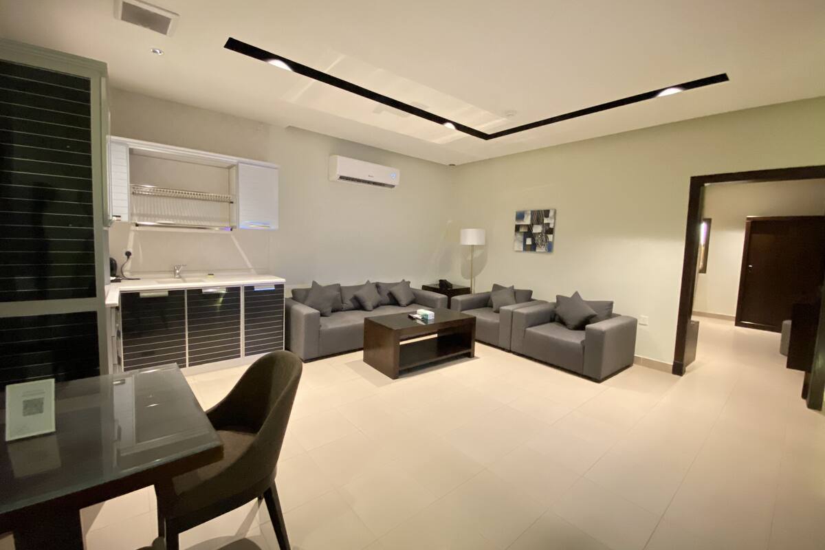 A modern living room with a sectional sofa, a glass coffee table, and a dining area with a table and chairs.