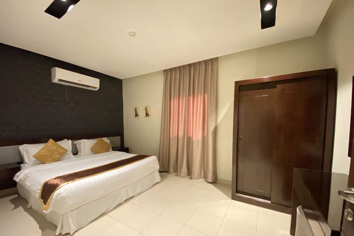 A hotel room with a large bed, a wardrobe, an air conditioning unit, and a television.