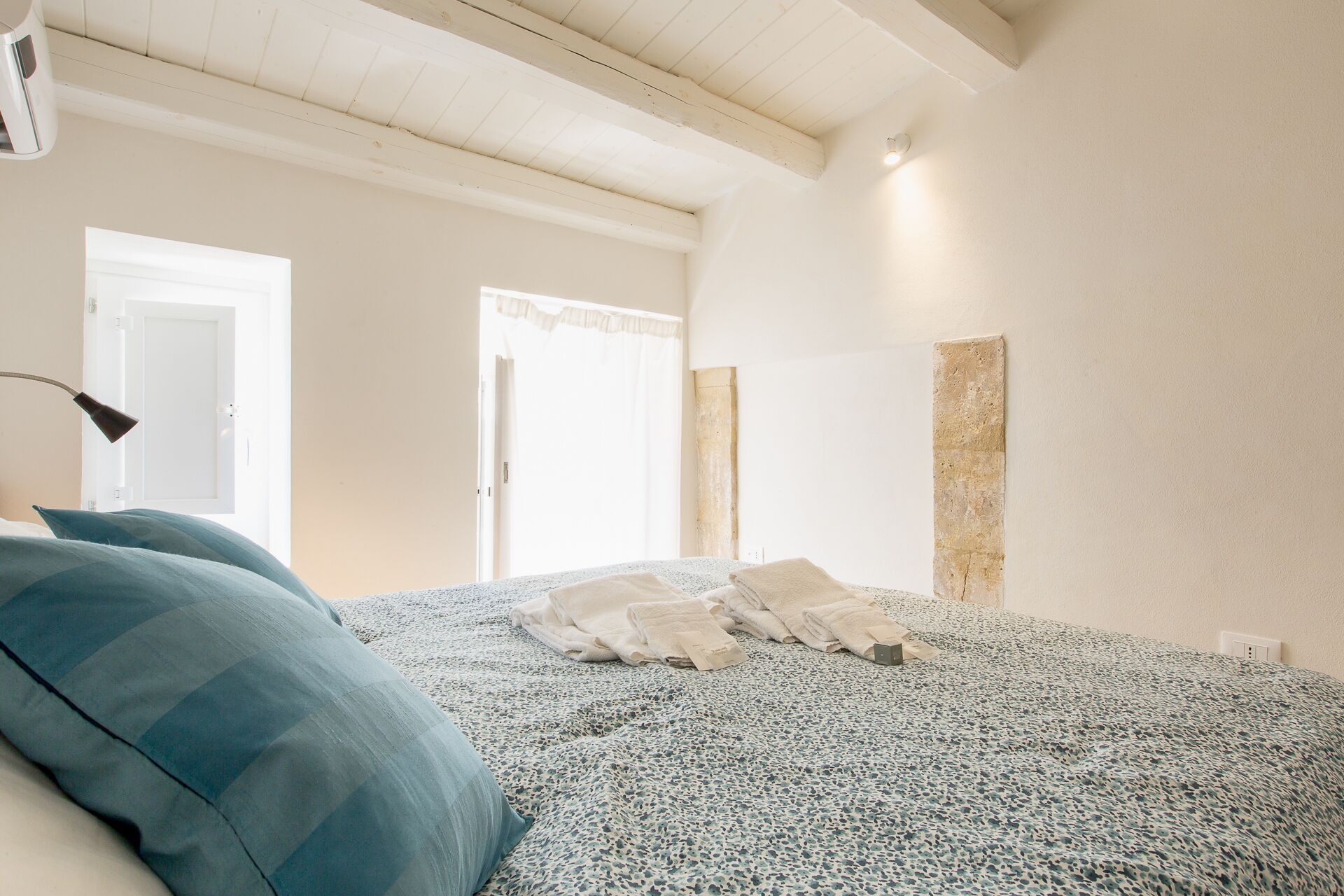 A bedroom with a bed, pillows, a lamp, and a door.