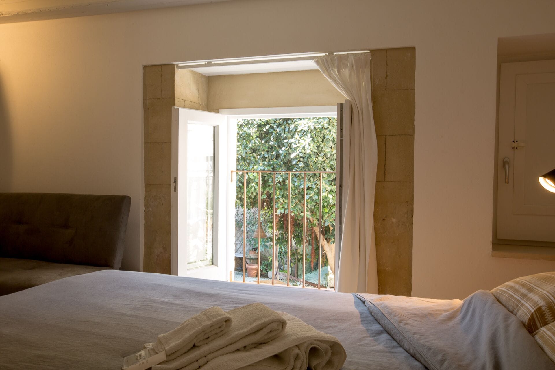 A hotel room with a bed, a view of a balcony with a railing, and a door leading outside.