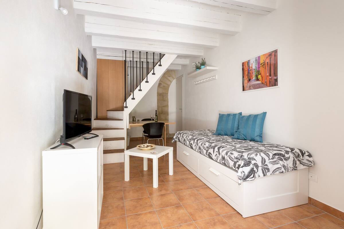 A compact living space with a bed, a TV, a dining area, and a staircase.