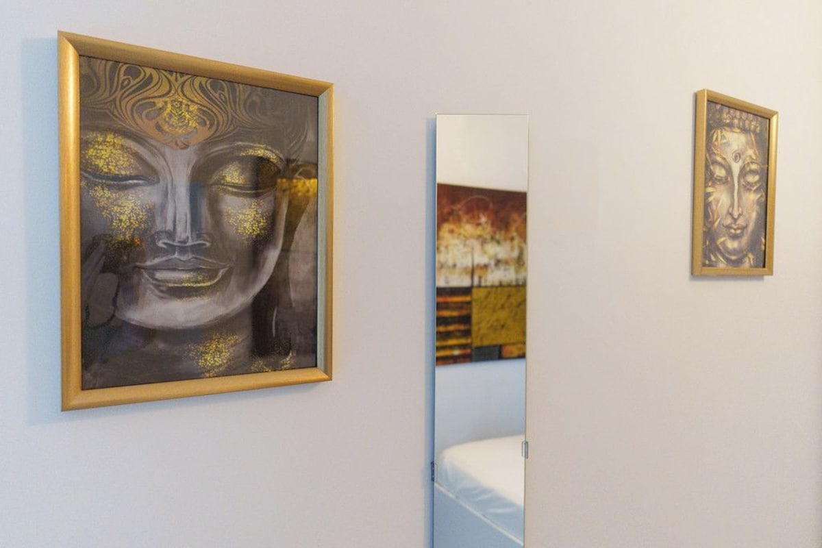 A room with a bed, a wall-mounted mirror, and two framed artworks.