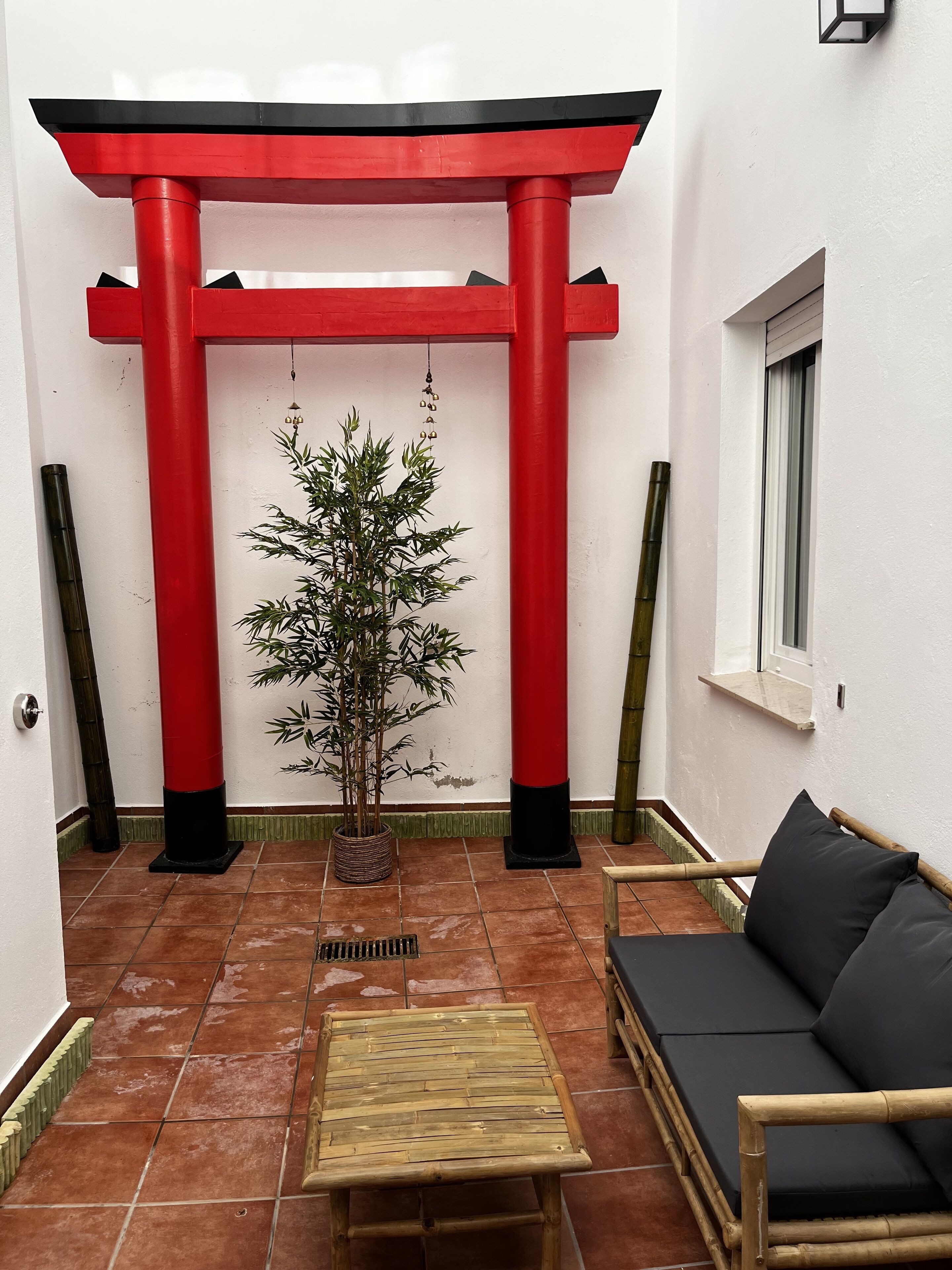 A room with a red torii gate, a bamboo plant, a wooden table, and a black sofa.