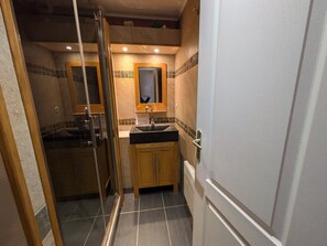 Un baño pequeño con ducha, lavamanos y espejo.