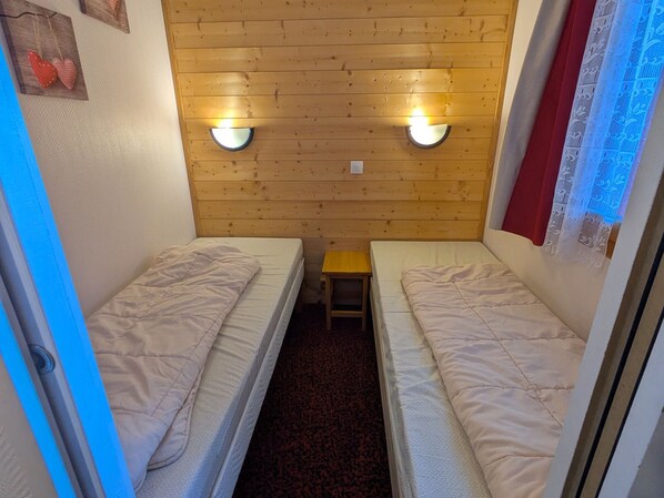 A small room with two single beds, a wooden wall, and two wall-mounted lights.