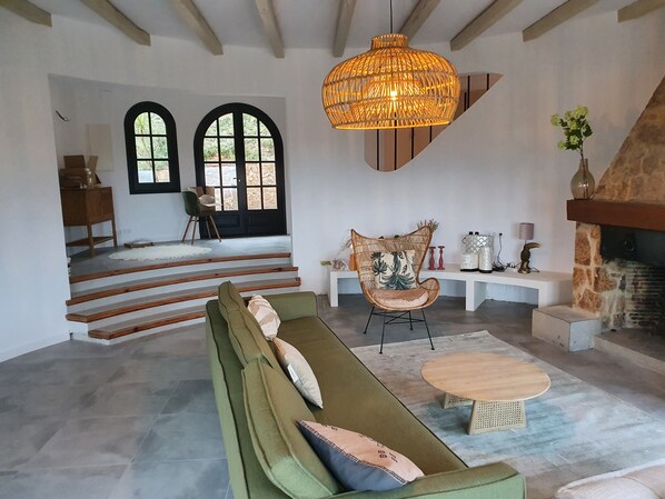 A spacious living area with a green sofa, a wicker chair, a wooden coffee table, a stone fireplace, and a large woven light fixture.
