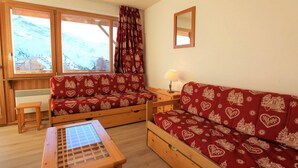 A cozy room with a wooden sofa and a small table, a window with curtains, and a mirror on the wall.