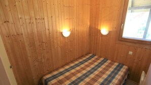 A small, single-bed room with wooden walls and two wall-mounted lights.