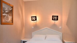 Une chambre à coucher avec un lit blanc, deux tables de chevet et deux lampes fixées au mur.