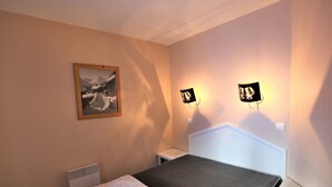 A single bed with a white headboard and a beige blanket, a small bedside table, a wall-mounted light fixture, and a framed picture on the wall. - Apartment for 4 people at the foot of the slopes with Wifi in Avoriaz (Avoriaz)