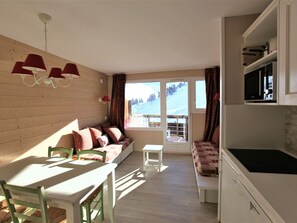 Een gezellige kamer met een houten wand, een eettafel met stoelen, een bank met decoratieve kussens en een keukenhoek met een fornuis.