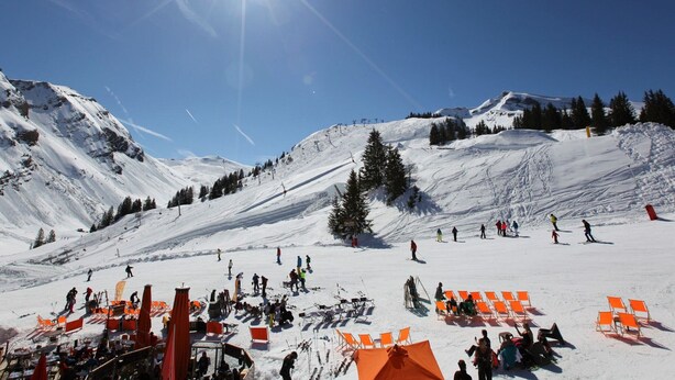 Une pente de montagne enneigée, avec des skieurs et un ciel dégagé.