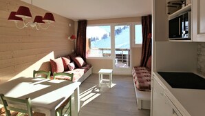 A cozy room with a wooden wall, a dining table with chairs, a sofa with patterned cushions, and a kitchen area with a stove. - Apartment for 4 people at the foot of the slopes with Wifi in Avoriaz (Avoriaz)