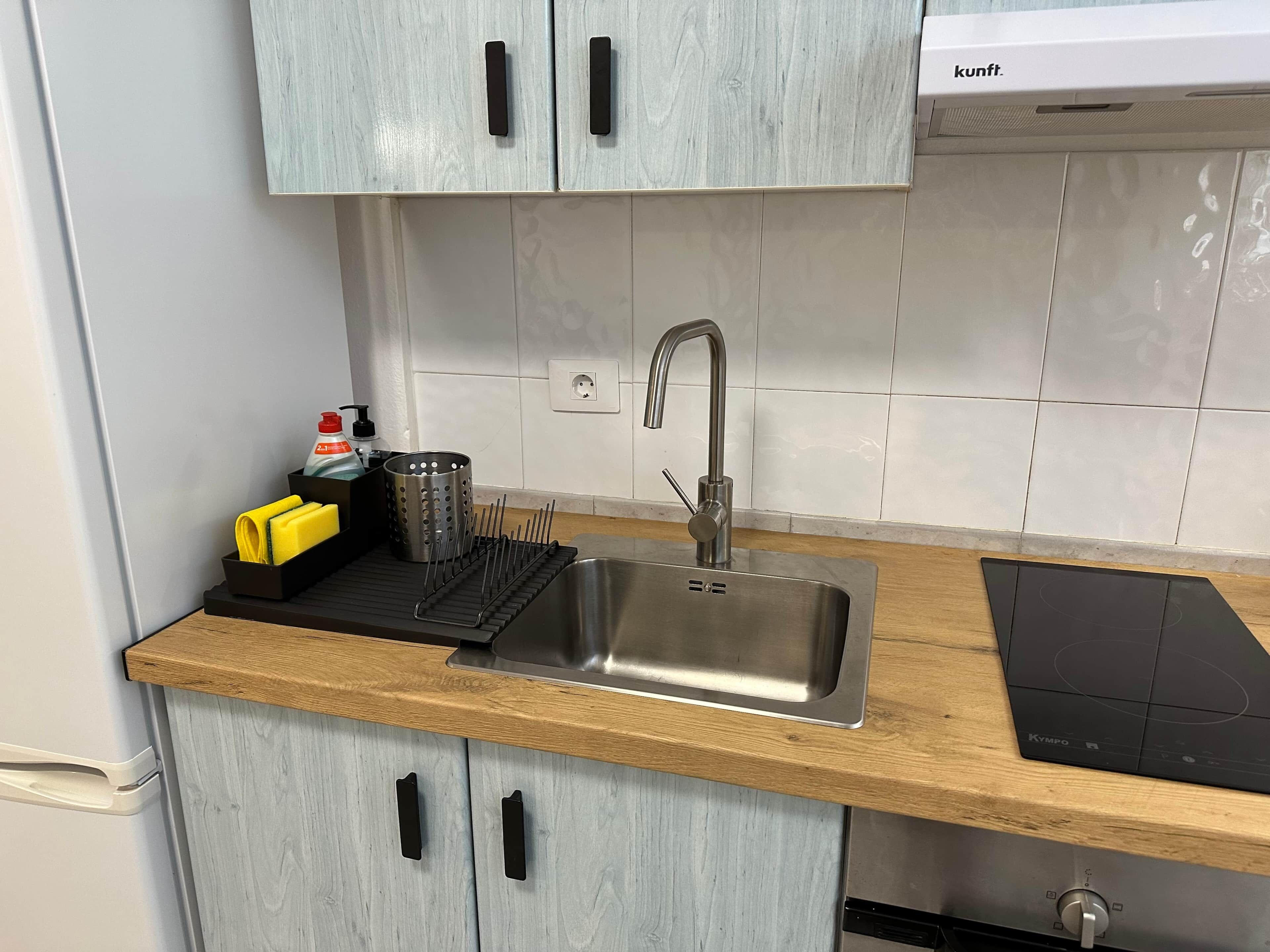 A kitchen with a stainless steel sink, wooden countertop, and light blue cabinets.