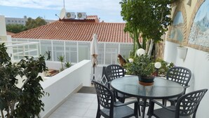 En tagterrasse med et rundt bord og stole, plantekrukker og udsigt til en bygning med røde tegltage.