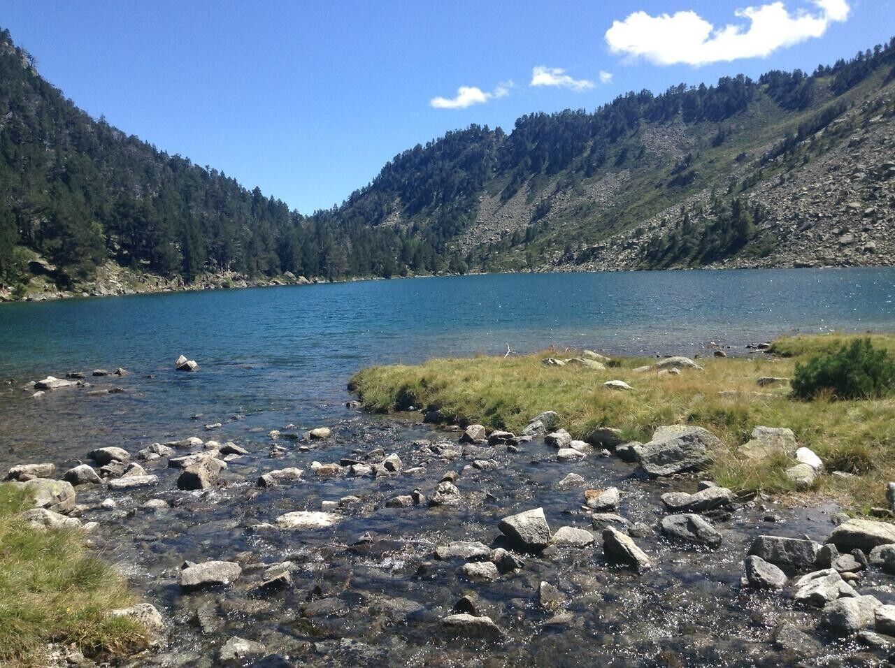 Un lac aux eaux limpides, entouré de reliefs rocheux et de collines boisées.