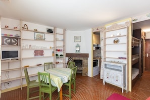 Un coin repas avec une table et des chaises, une cheminée, une cuisine équipée d’une cuisinière et un lit superposé dans la pièce adjacente.