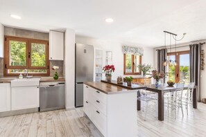 A modern kitchen with white cabinetry, a stainless steel refrigerator, and a dining area with a wooden table and chairs.