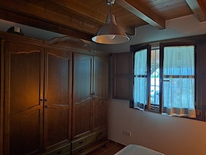 A room with wooden cabinets, a hanging light fixture, a window with curtains, and a white bedspread.