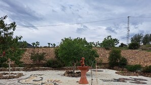 Ein Garten mit einer zentralen Terrakotta-Fontäne, umgeben von Kieselsteinen und Steinen, mit einer Steinmauer und Kakteen im Hintergrund.